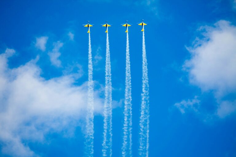 Four planes leaving trails behind them, streak across the sky flying in a row.
